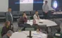 Attendees around tables in discussion, one standing, with refreshments at the back of the room.